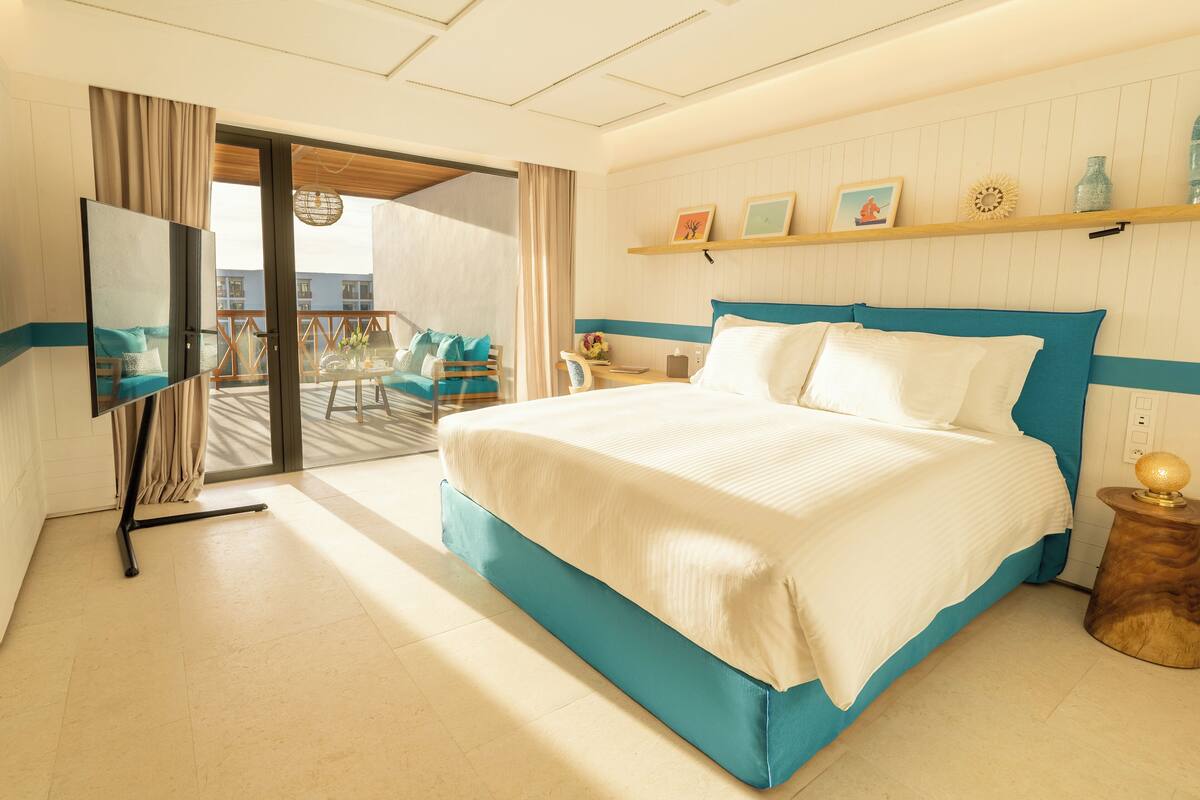 Une chambre d’hôtel avec un lit, une télévision, un balcon avec des chaises et une vue sur la ville.