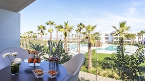 A balcony with a table set for a meal, overlooking a pool and palm trees. - The View Bouznika (El Mansouria)