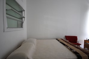 A simple room with a bed, a red chair, and a window with blinds.