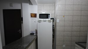 Una cocina compacta con un refrigerador blanco, un microondas encima y un salpicadero de azulejos.
