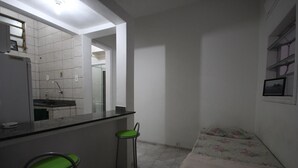 Habitación pequeña y funcional con kitchenette, una cama y dos sillas verdes.