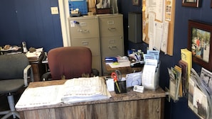 A reception desk with a wooden finish, a chair, a bulletin board with papers, and a filing cabinet. - Indian Beach Resort (Clearlake Oaks)
