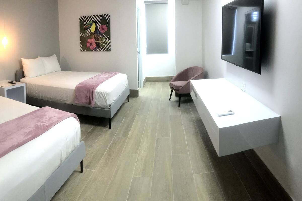 A hotel room with two beds, a desk, a chair, a flat-screen TV, and a wall-mounted artwork.
