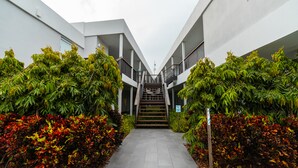 Un edificio moderno con una escalera central, rodeado de abundante vegetación y un sendero pavimentado.