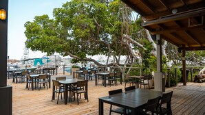 Un espacio de comedor al aire libre con mesas y sillas de madera, con vistas a un puerto deportivo con barcos.