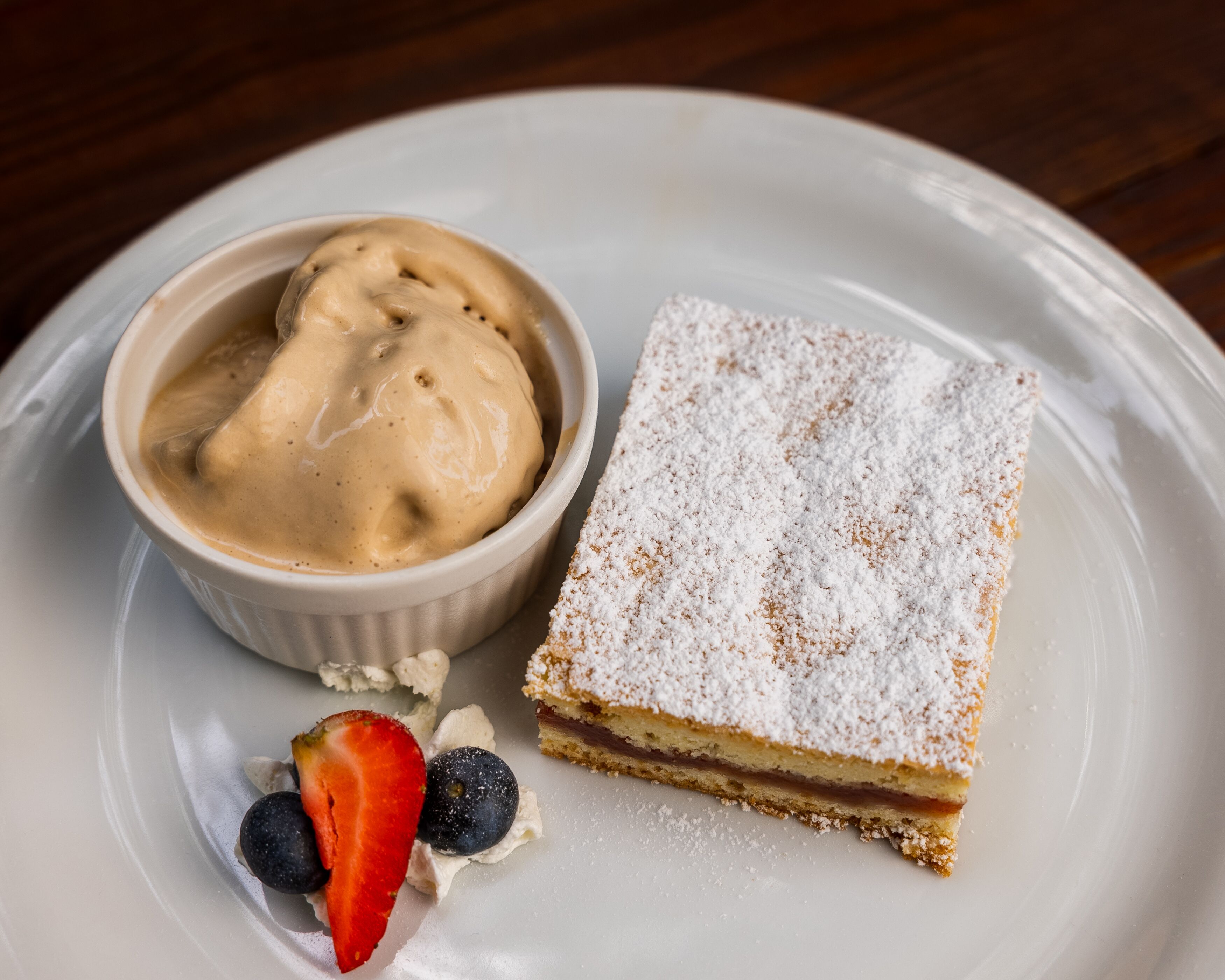 A dessert plate with a slice of cake dusted with powdered sugar, a scoop of vanilla ice cream, and fresh berries.
