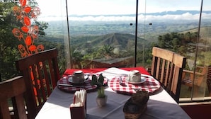 A table set with a red and white checkered tablecloth, two cups, a small potted plant, and a decorative item on a balcony with a scenic view.