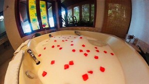 A bathtub filled with water and red rose petals, with a window and a plant visible in the background.
