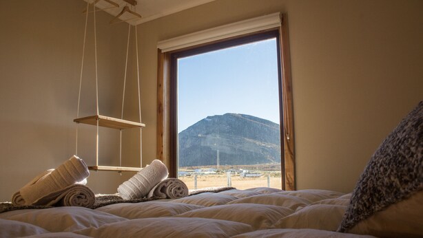 Ein Schlafzimmer mit Bett, einer hängenden Ablage und Blick auf einen Berg durch ein Fenster.