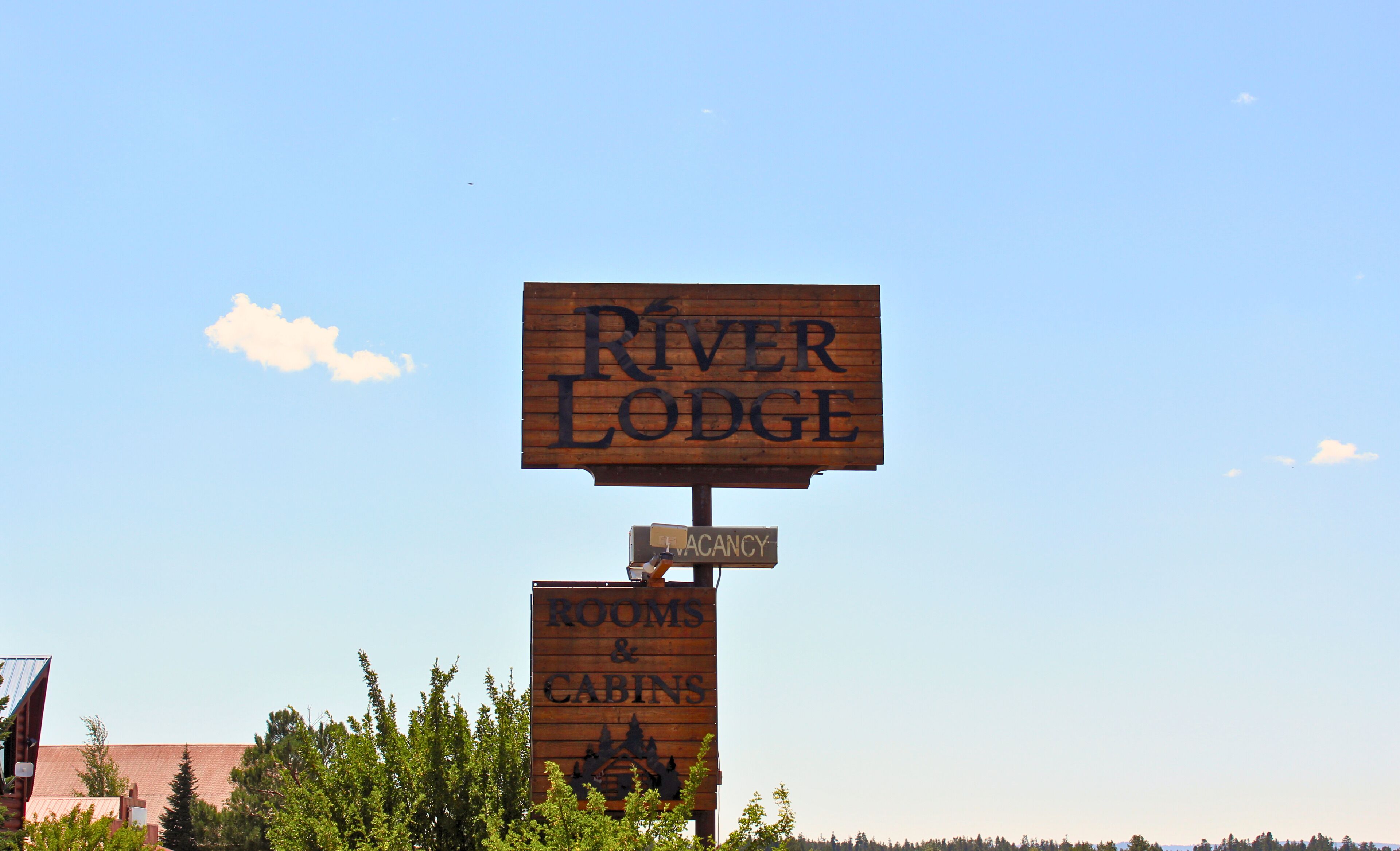 A wooden sign for River Lodge indicating rooms and cabins available for rent.