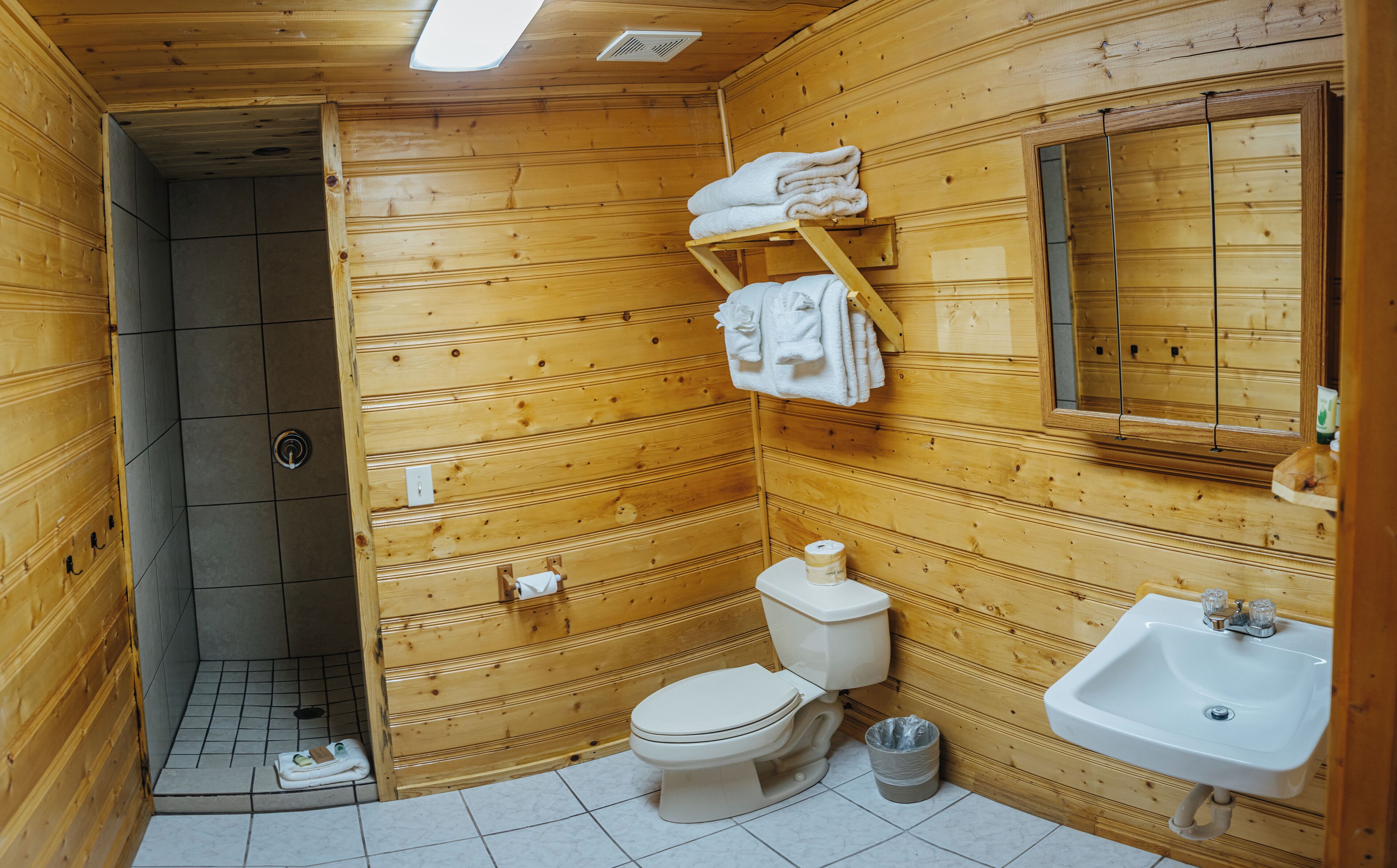 A wooden cabin bathroom with a toilet, sink, and shower.