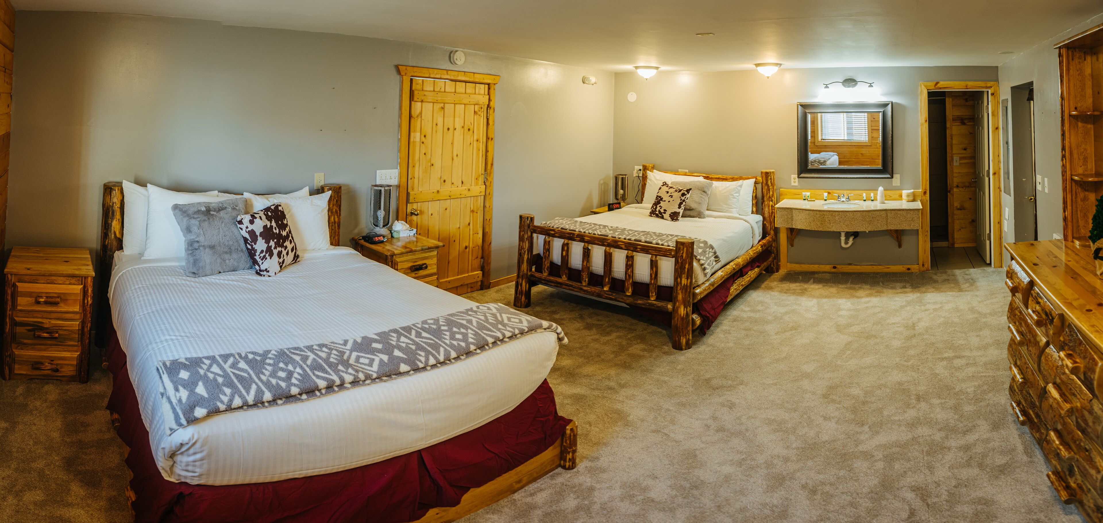 A bedroom with two beds, a wooden wardrobe, a vanity with a mirror, and a wooden dresser.
