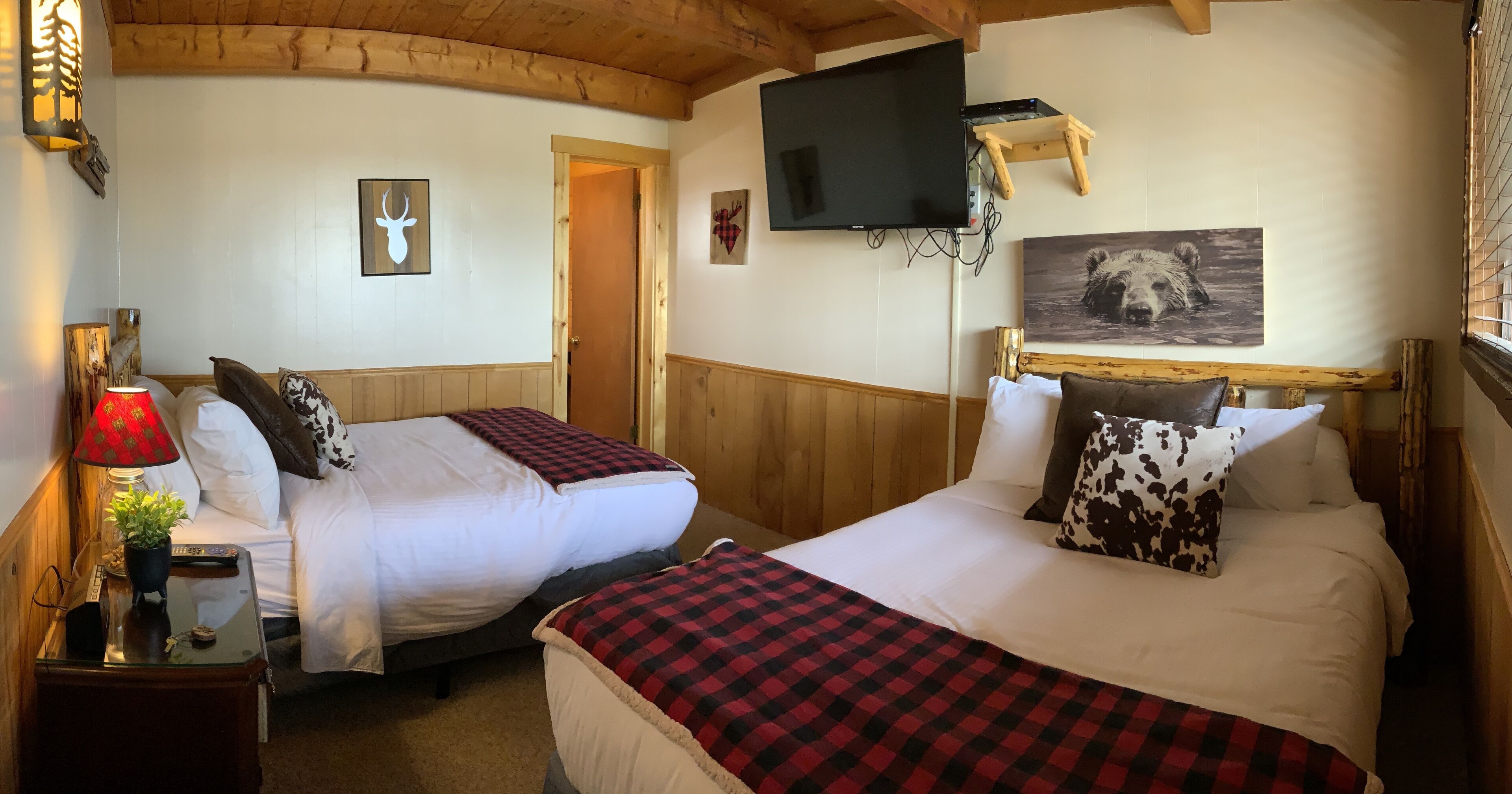 A cozy room with two beds, a TV mounted on the wall, and a wooden ceiling.