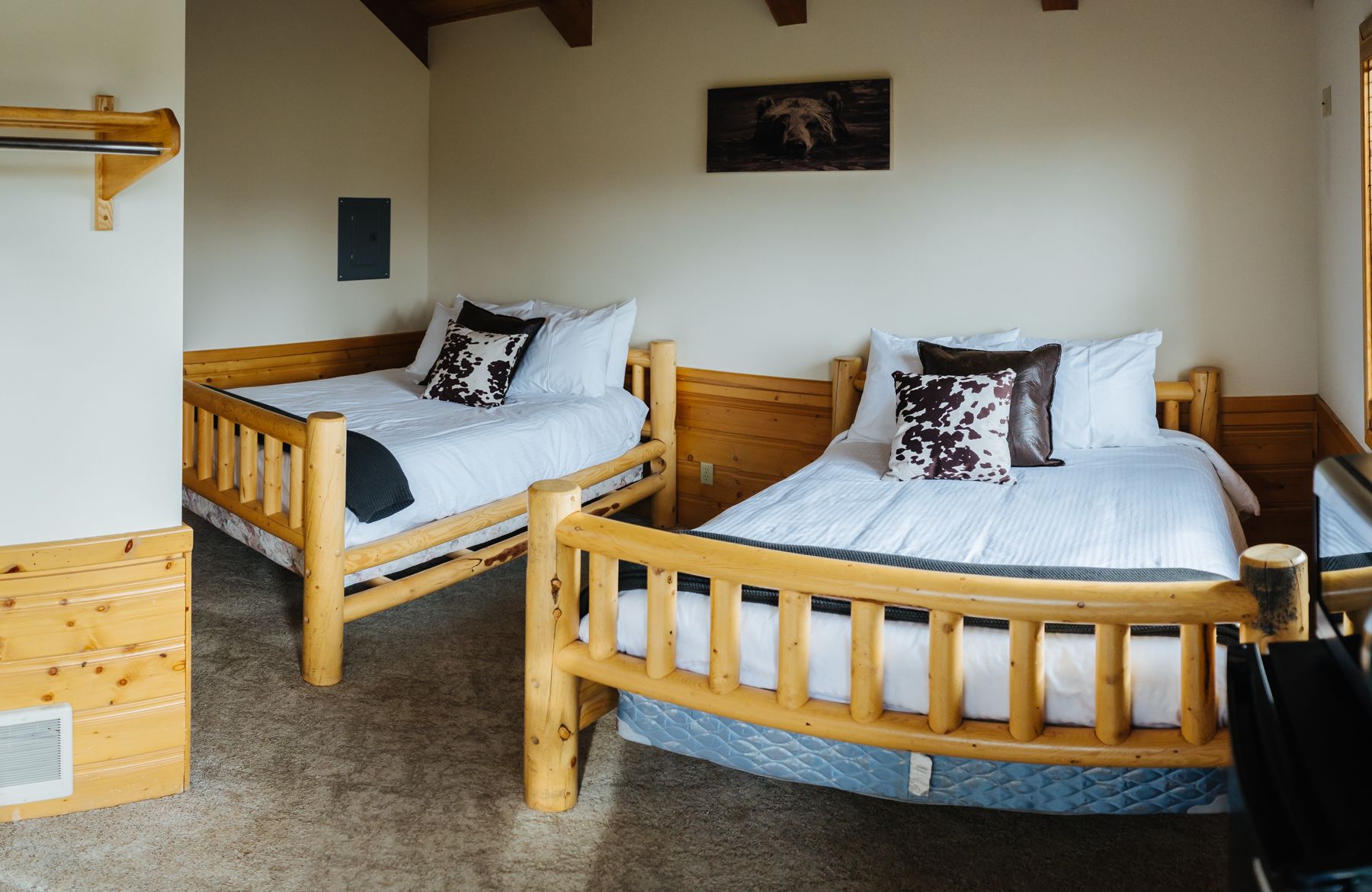 Dos camas litera de madera con ropa blanca de cama y almohadas estampadas, un cabecero de madera y un pequeño aparador de madera.