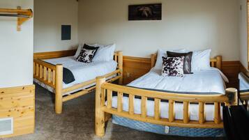 Two wooden bunk beds with white bedding and patterned pillows, a wooden headboard, and a small wooden dresser.