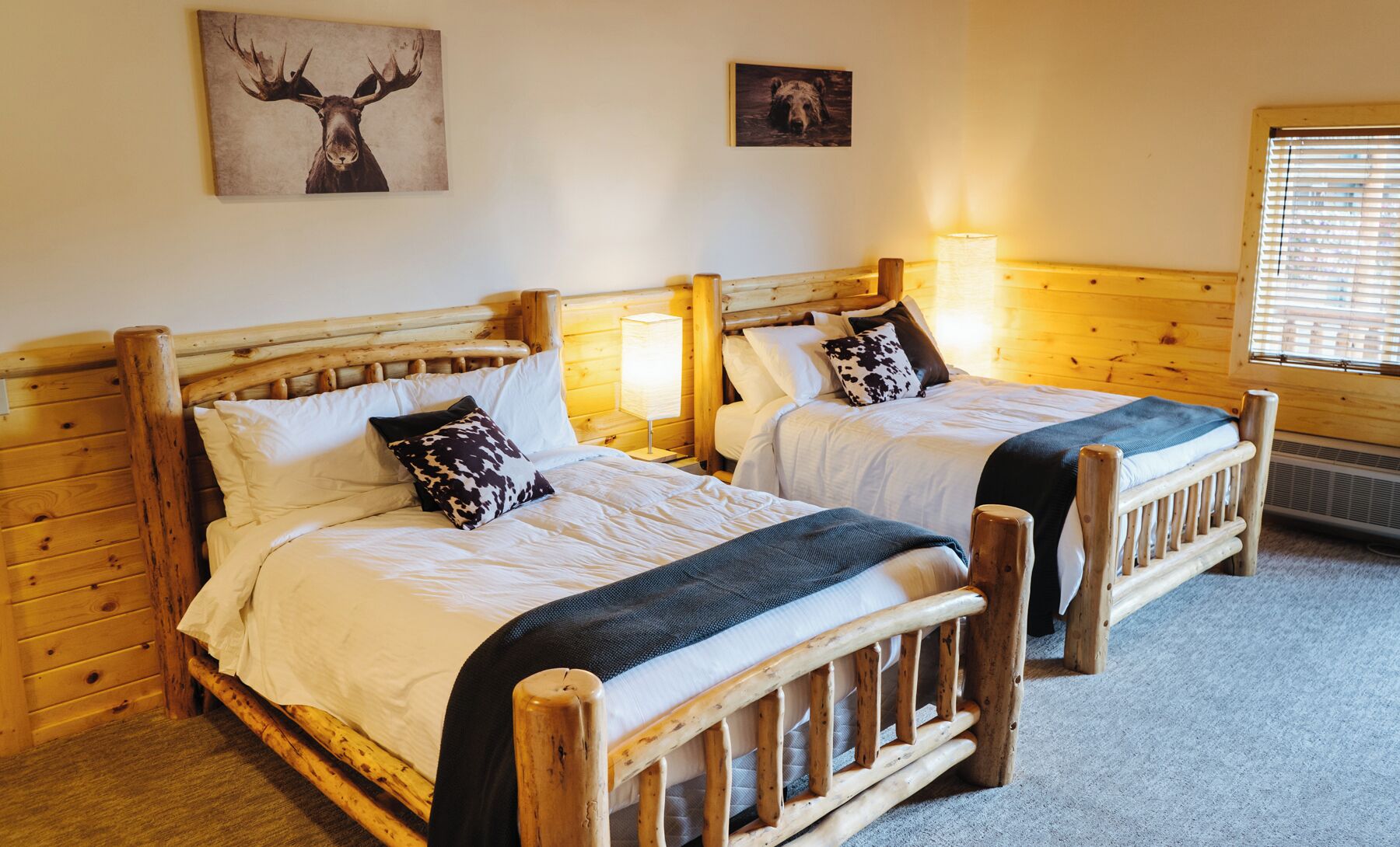 Two wooden beds with white linens and patterned pillows, a wooden headboard, and a lamp on each bed.