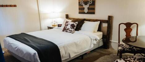 A neatly made bed with a white and black blanket, a wooden headboard, and a deer head artwork above it.