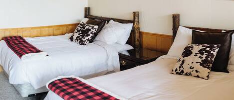A hotel room with two beds, each with white bedding and a red and black checkered throw blanket. There are wooden headboards and a wooden beam ceiling.