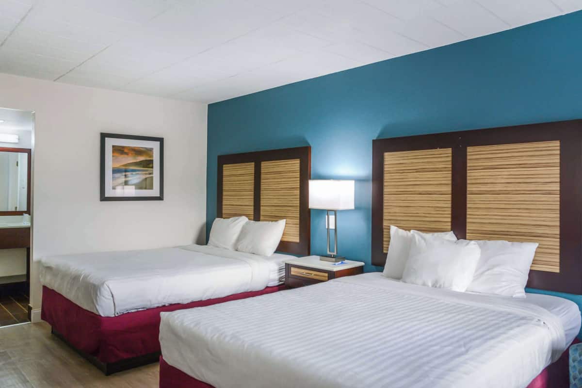 A hotel room with two beds, a nightstand, a lamp, and a framed picture on the wall.