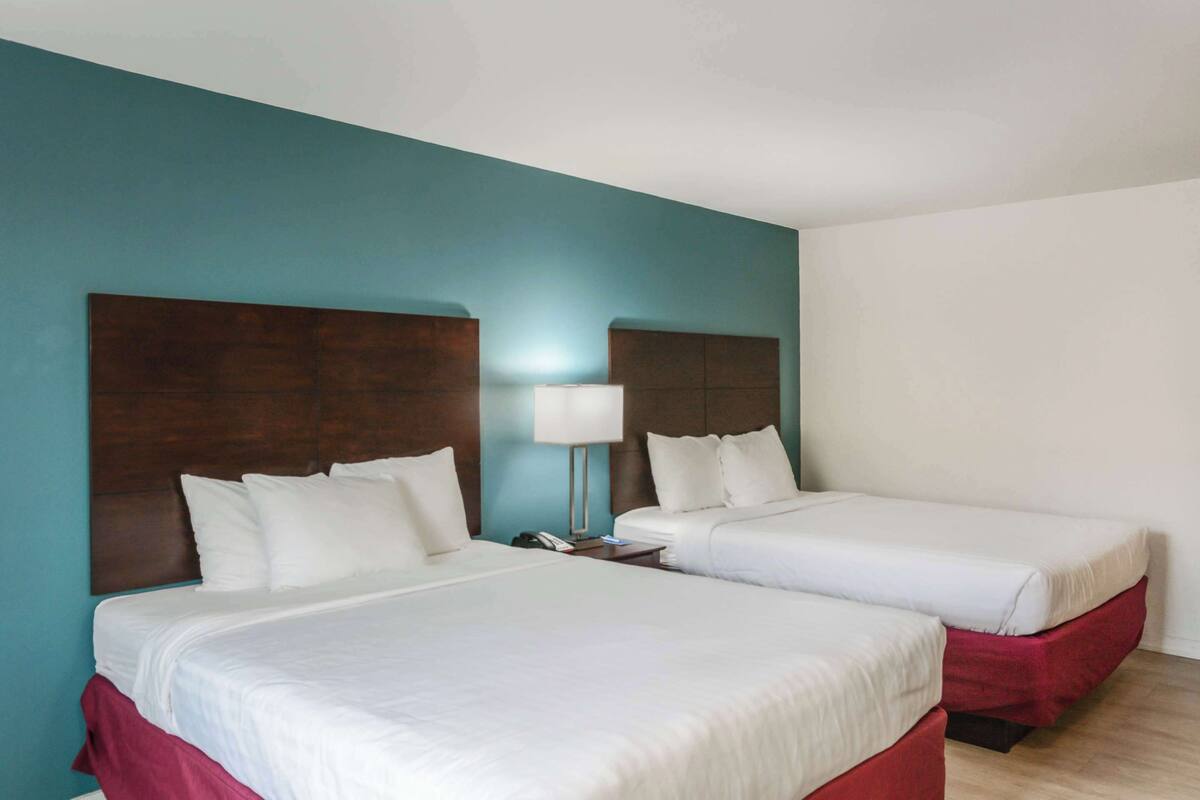 A hotel room with two beds, a nightstand, and a lamp.
