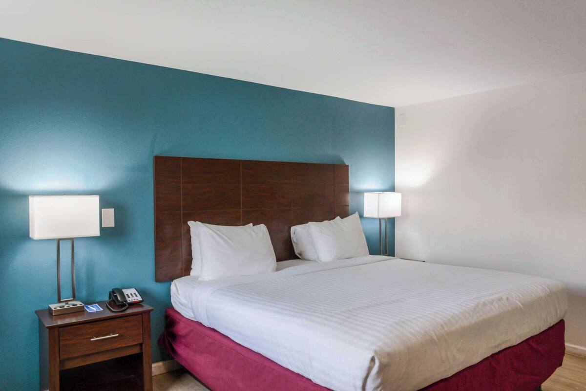 A hotel room with a large bed, two bedside lamps, a wooden headboard, and a nightstand with a phone and a lamp.