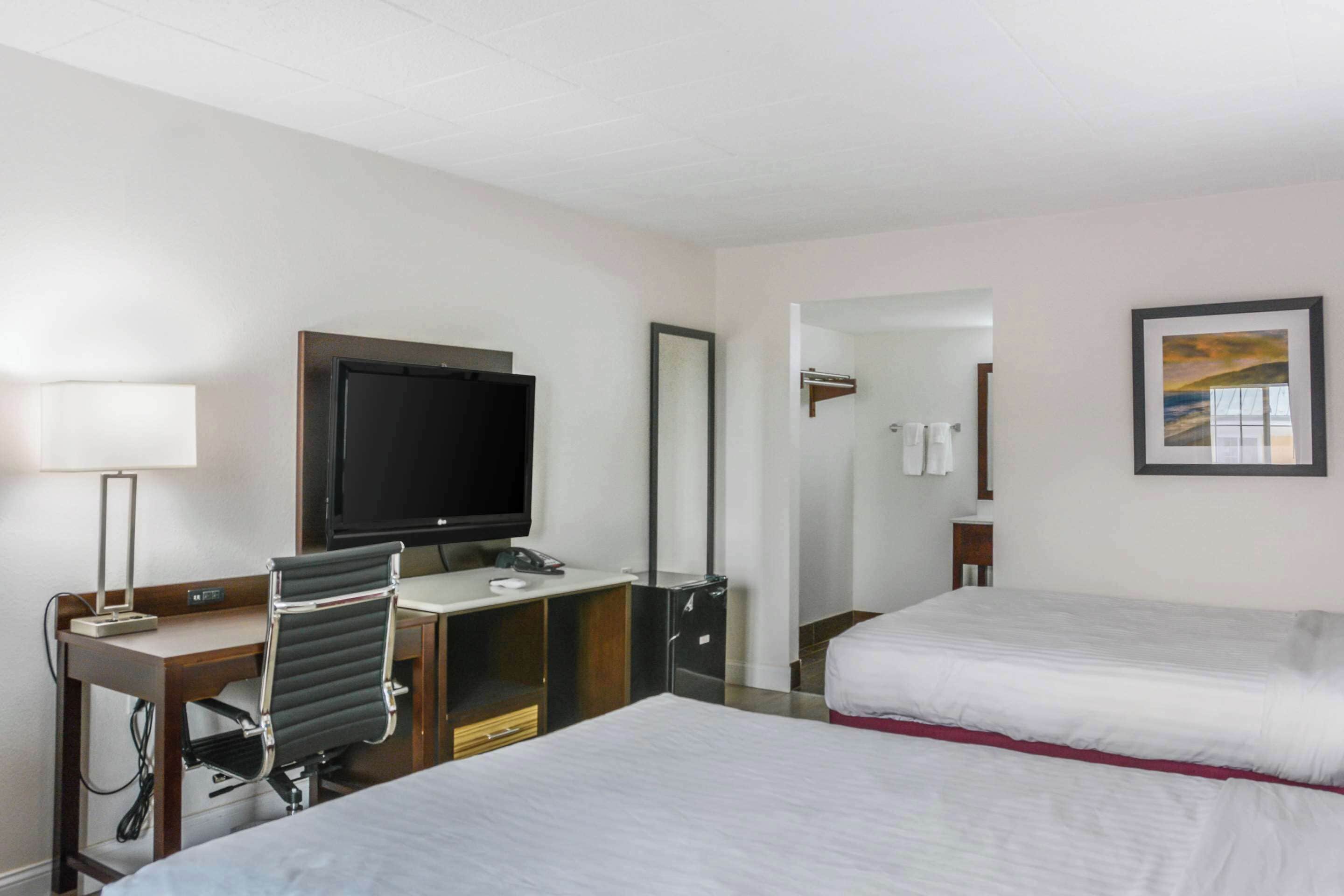 Una habitación de hotel con cama, escritorio, silla, televisor y espejo.
