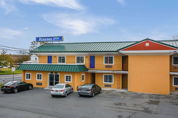 A two-story motel with a green roof and a sign that reads "Rodeway Inn." There are three cars parked in front.