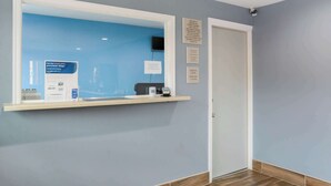 Une salle d’attente avec un mur bleu, une porte blanche et un comptoir d’accueil doté d’un ordinateur et d’une petite horloge.