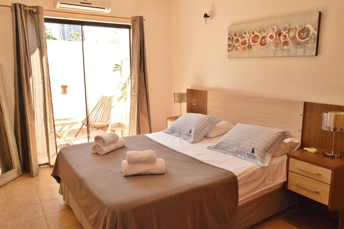A hotel room with a large bed, a bedside table with a lamp, and a view of the outside balcony.