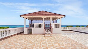 A gazebo with a tiled floor and a railing, overlooking a beach with the ocean in the background. - Scarlett Guesthouse Hotel Resorts (Bull Bay)