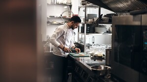 A chef preparing food in a professional kitchen with stainless steel appliances and organized shelves. - Scarlett Guesthouse Hotel Resorts (Bull Bay)