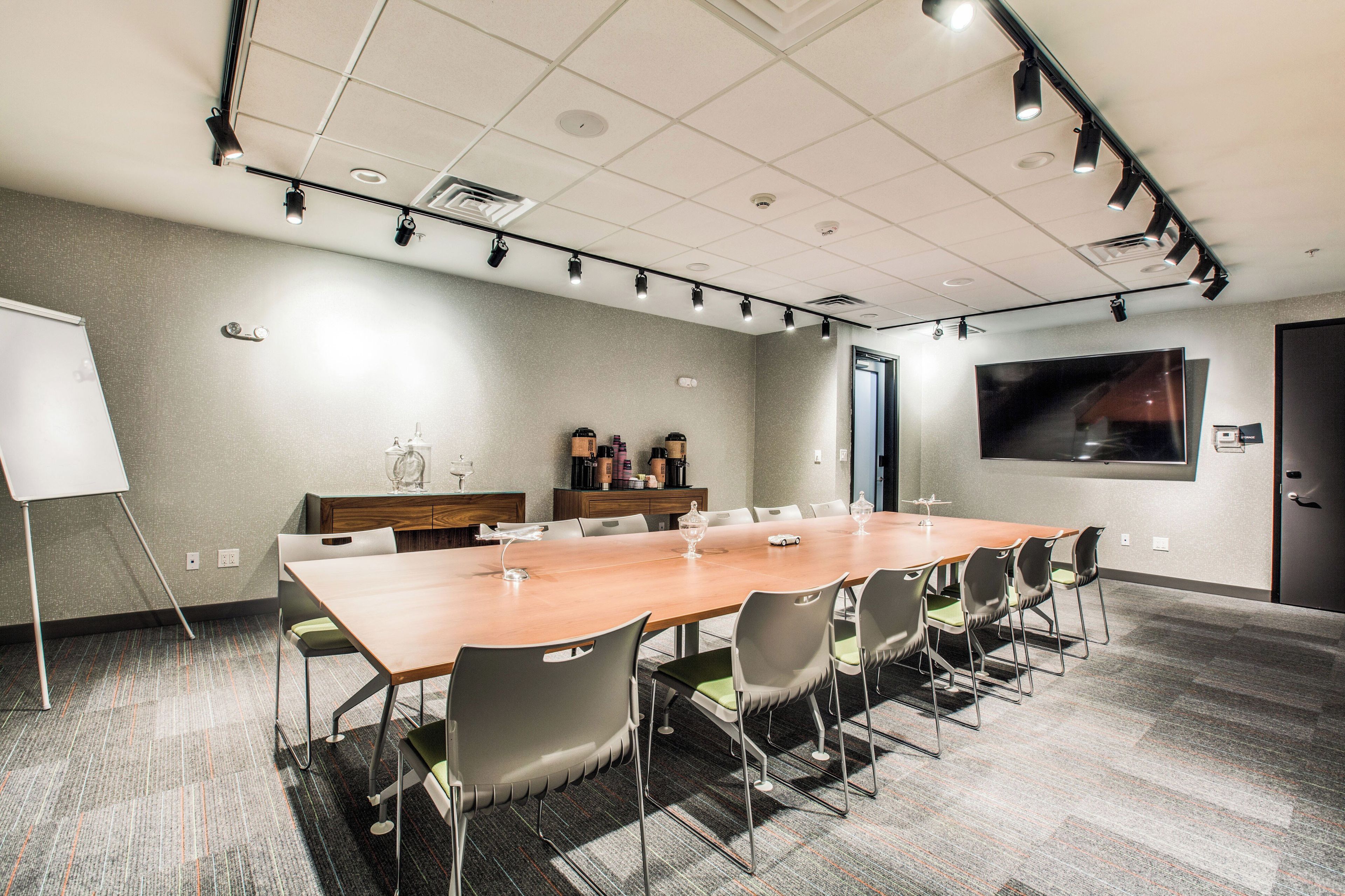 A conference room with a long table, chairs, a whiteboard, and a television screen on the wall.