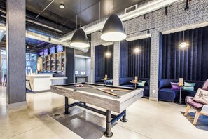 A pool table in a modern lounge area with overhead lighting and a bar in the background. - Aloft by Marriott Dallas Arlington Entertainment District (Arlington)