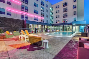 A hotel courtyard with a pool, lounge chairs, and a stone wall. - Aloft by Marriott Dallas Arlington Entertainment District (Arlington)