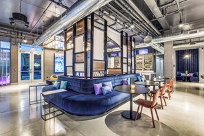 A modern lounge area with a curved blue sofa, a round table, and orange chairs. - Aloft by Marriott Dallas Arlington Entertainment District (Arlington)