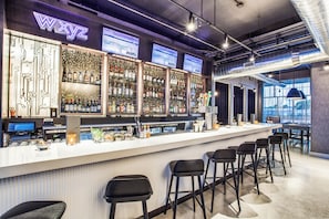 A bar area with a long counter, multiple shelves of bottles, and bar stools.