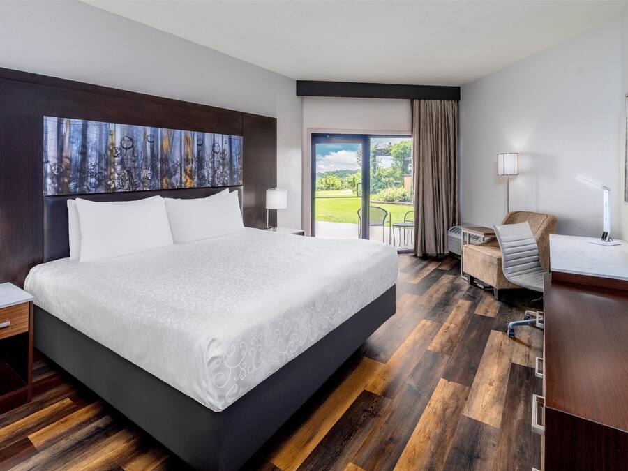 A modern hotel room with a large bed, a desk, a chair, and a view of the outdoors.