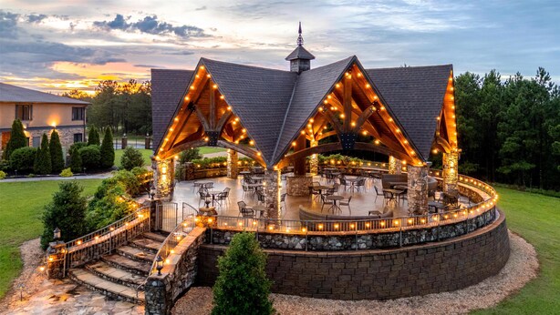 A circular outdoor patio with stone walls and wooden beams, surrounded by a stone walkway and steps leading to a covered seating area.