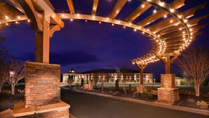 A well-lit entrance with a wooden pergola and stone pillars, leading to a building with a dome-shaped structure.