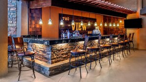 A bar area with a stone wall, wooden ceiling, and multiple hanging light fixtures.