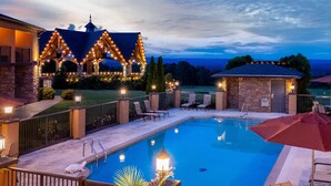 A swimming pool with a view of a house with lights, a covered patio, and a small building.