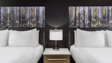 Habitación de hotel con dos camas, una mesita de noche con lámpara y dos cuadros abstractos en las paredes.