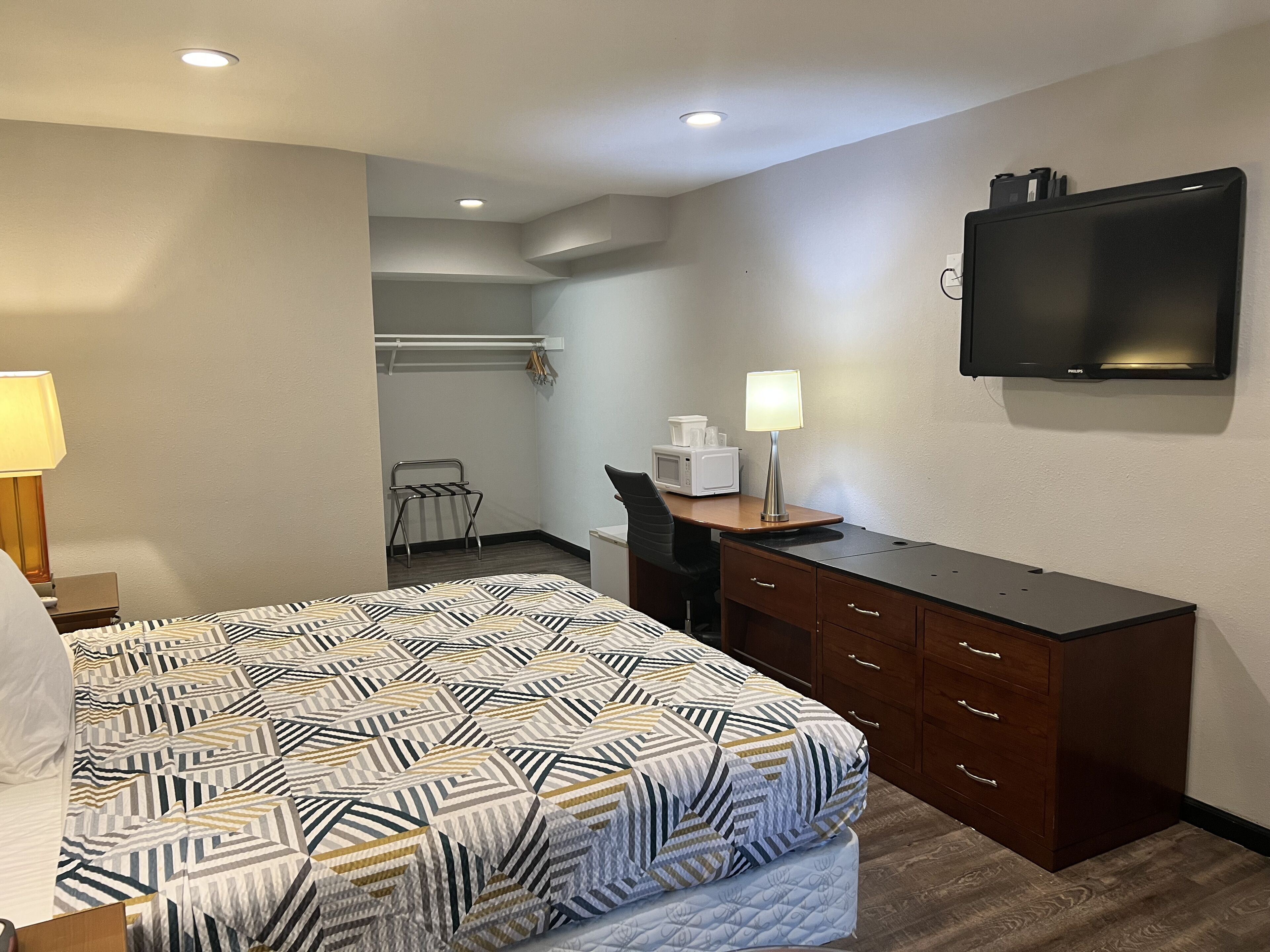 A hotel room with a bed, a desk, a chair, a television, and a lamp.