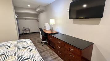 Una habitación de hotel con cama, escritorio con lámpara, silla, televisor y microondas.
