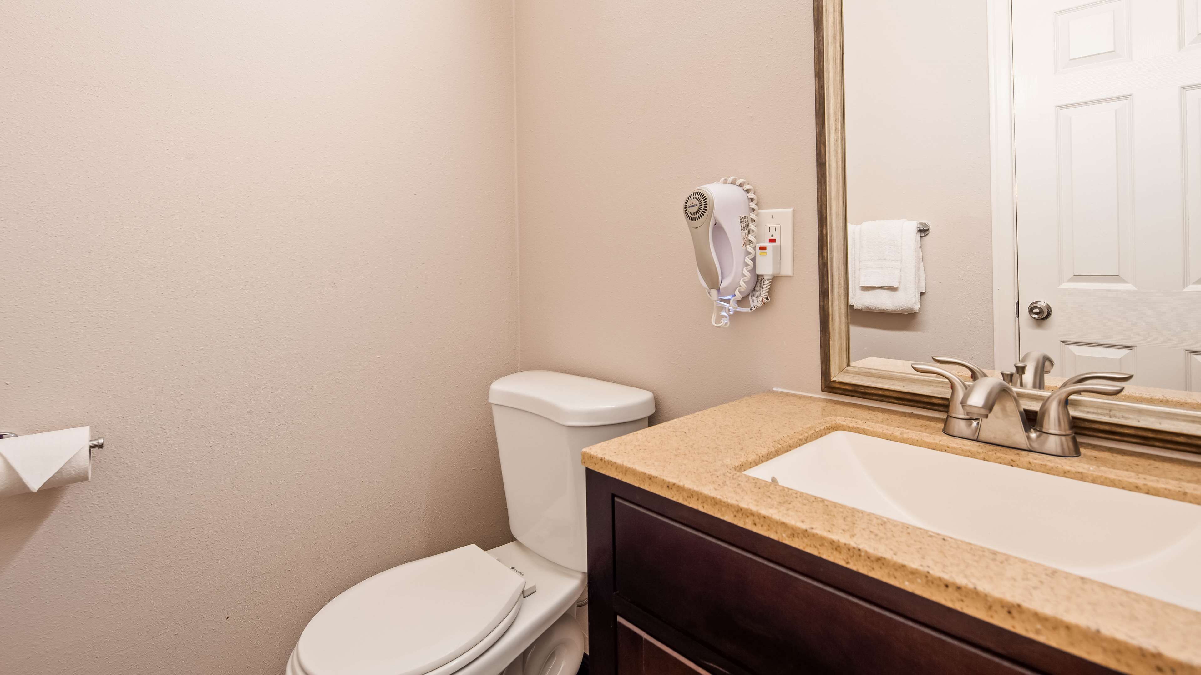 A bathroom with a white toilet, a sink with a dark countertop, and a mirror above the sink.