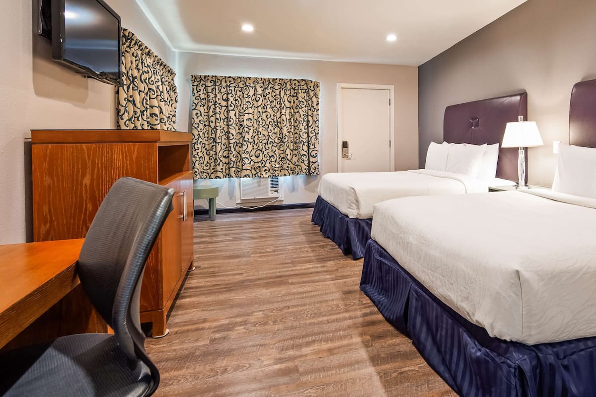 A hotel room with two beds, a desk, a chair, a TV, and a patterned curtain.