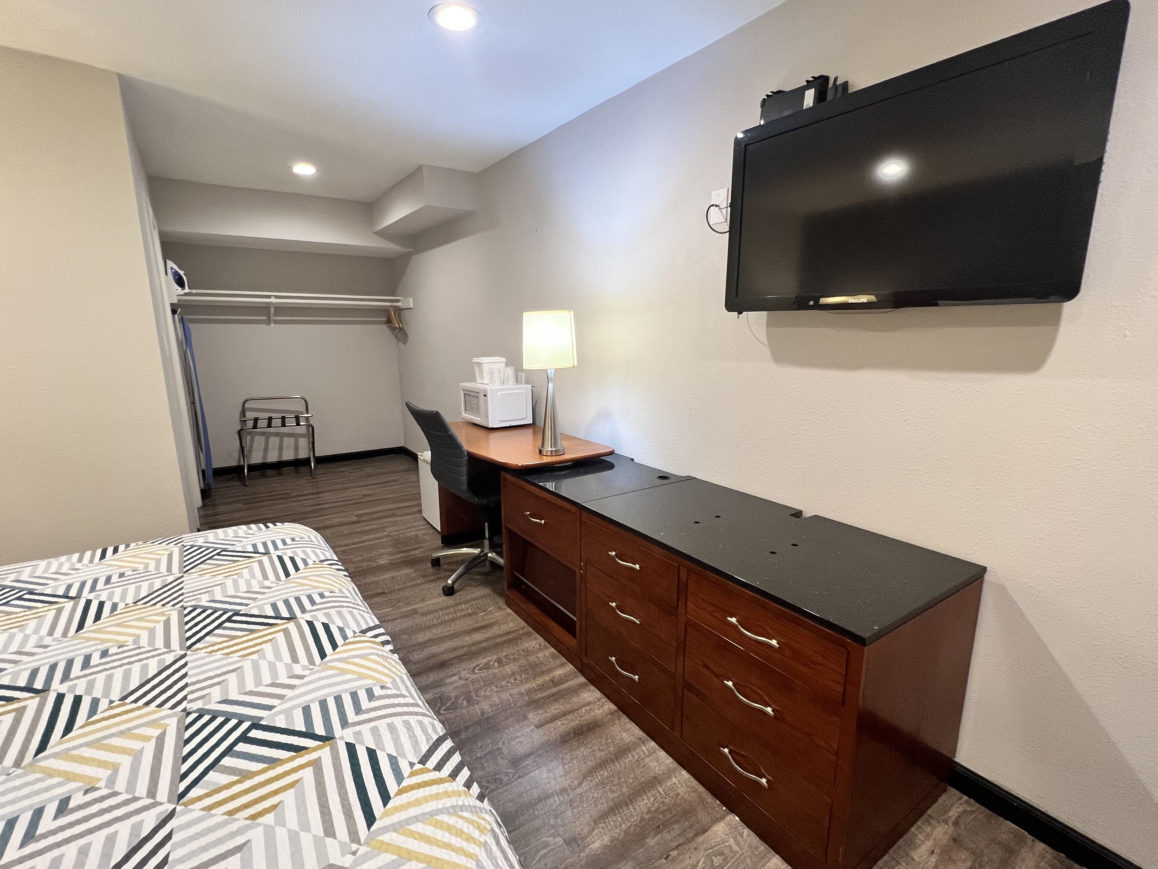 A hotel room with a bed, a desk with a lamp, a television, and a closet.