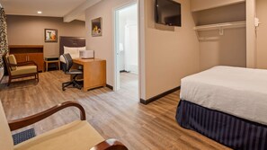 A hotel room with a bed, a desk, a chair, a TV, and a wardrobe.