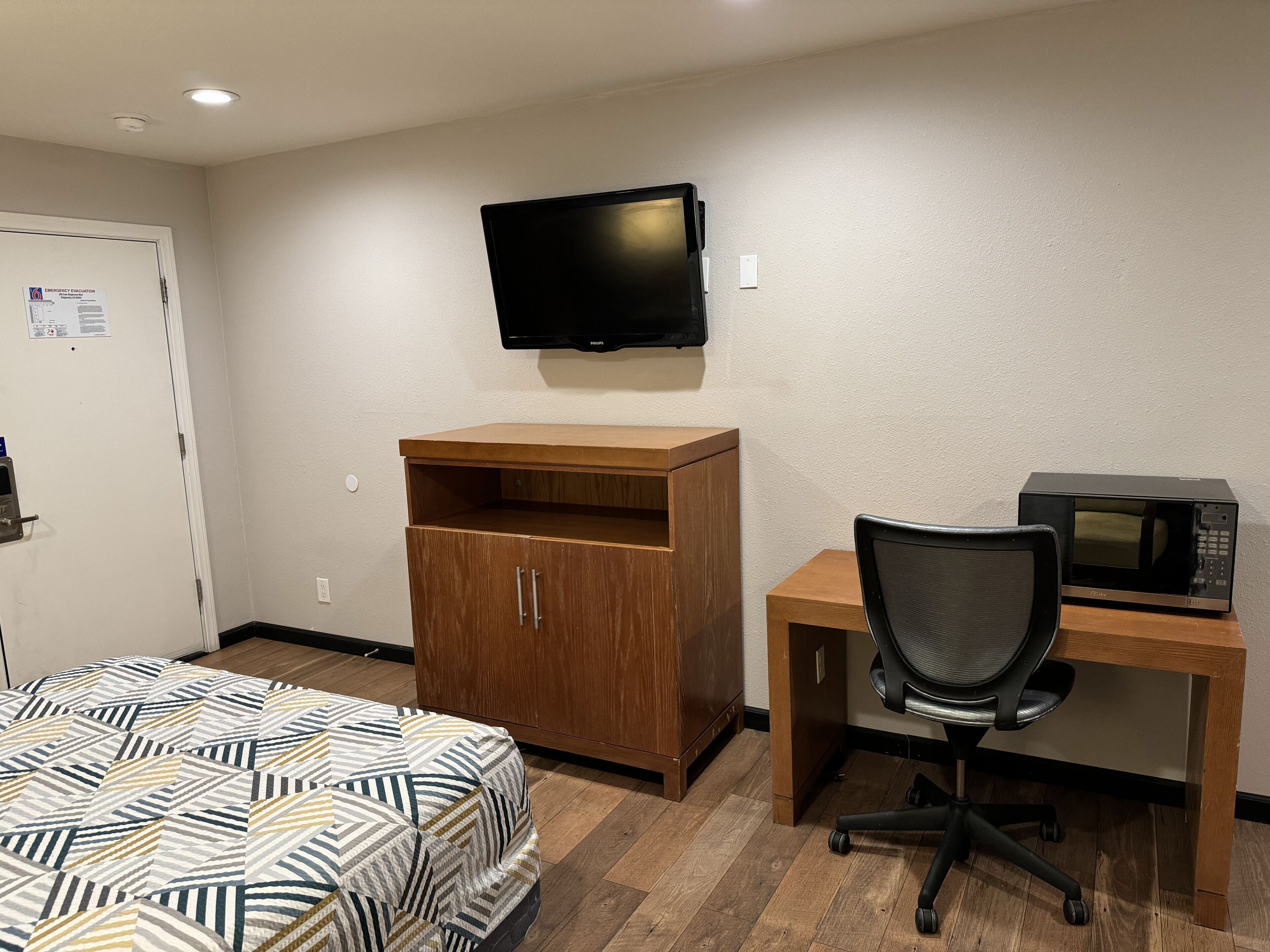 A hotel room with a bed, a wooden desk with a chair, a television, and a microwave.