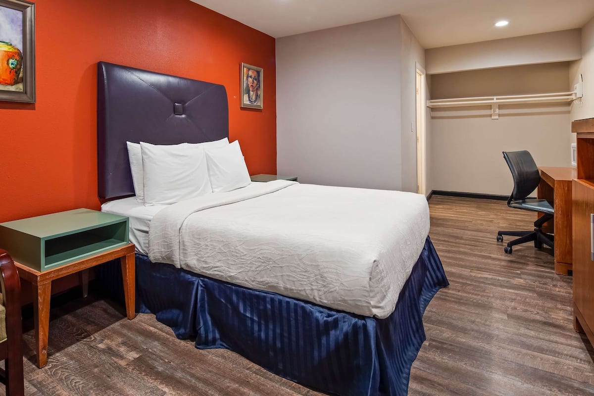 A hotel room with a bed, a desk, a chair, and a painting on the wall.